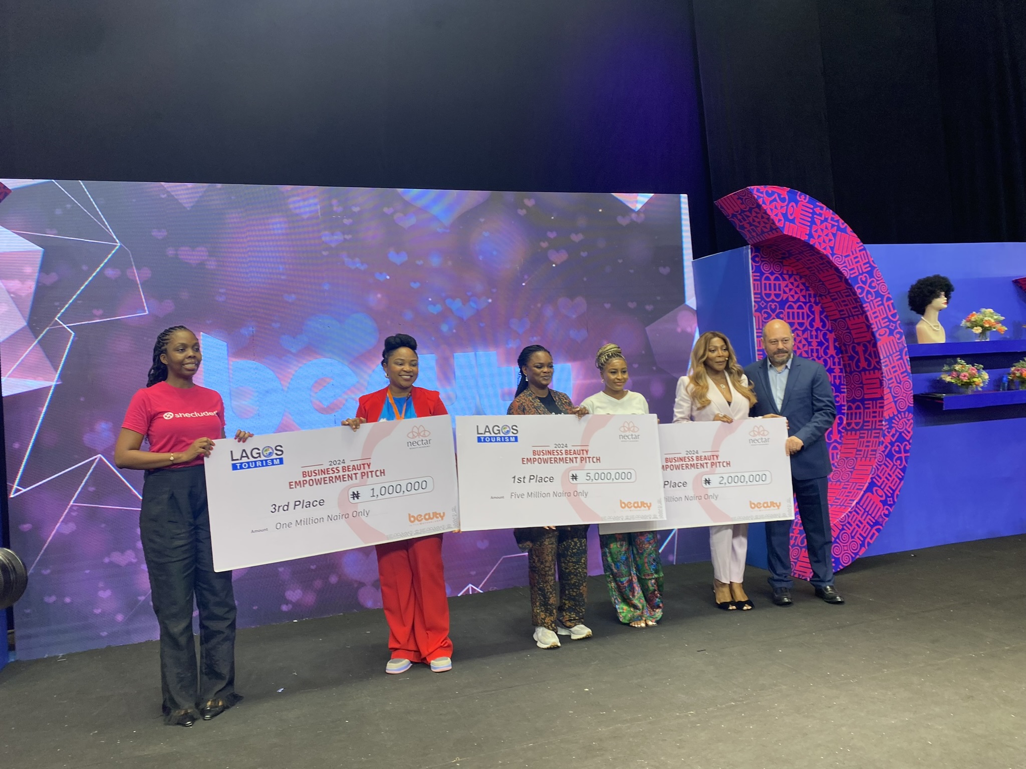 Three hard working women holding up their jumbo checks from the beauty in the motherland pitch competition.